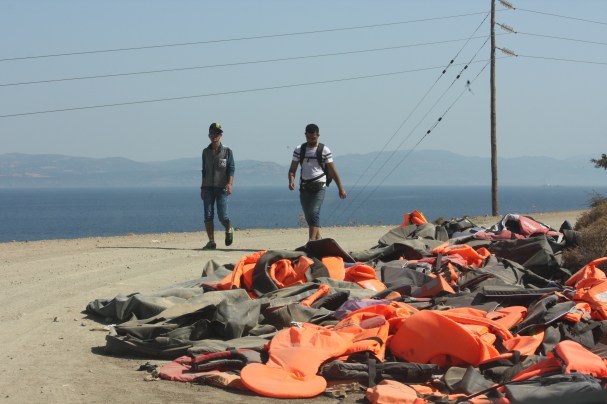 Refugees walk past discarded lifejackets on the road from Eftalou to Mytilini